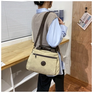 Model wearing a beige canvas shoulder bag with brown straps and a vintage logo