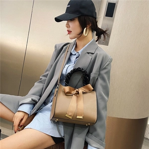 Sac à main kaki élégant avec grand nœud et poignée tressée porté par un modèle
