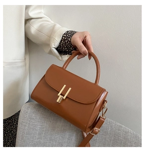 Macro detail of caramel brown leather handbag with a prominent golden metallic clasp buckle