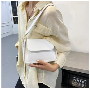 Close-up of white leather baguette bag worn by a model in a minimalist setting