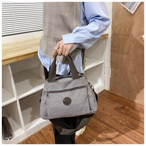 Detail of grey canvas travel bag with round leather logo and durable shoulder strap