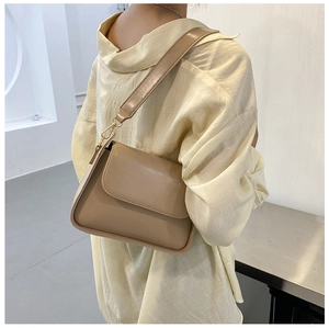 Close-up of a minimalist khaki PU leather baguette bag with a wide strap on model