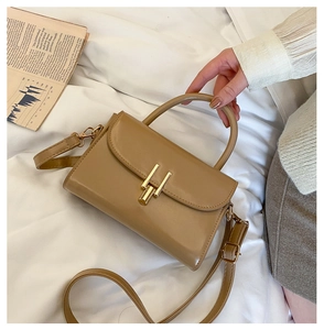 Detail of khaki leather handbag featuring a prominent gold metal buckle and handle