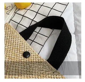 Close-up of straw woven beach bag featuring black fabric handle and snap closure detail