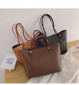 Trois grands sacs cabas minimalistes en marron et noir exposés sur une table en bois