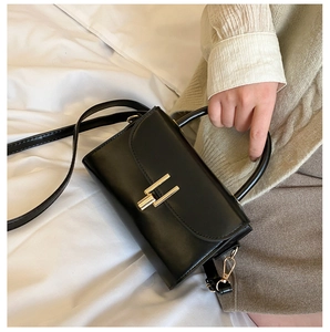 Close-up of black leather square handbag featuring a polished gold H-shaped buckle clasp
