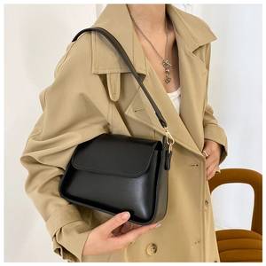 Detail of minimalist black leather baguette bag with gold metal buckle on khaki trench coat