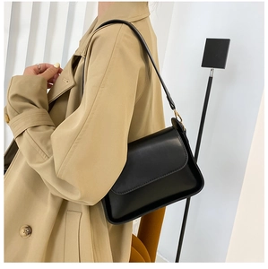 Close-up of black leather baguette bag with gold hardware worn over a khaki trench coat