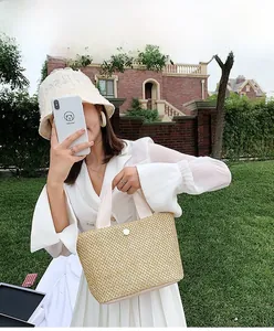 Detail of straw woven handbag with white button and cream handles on a grassy background