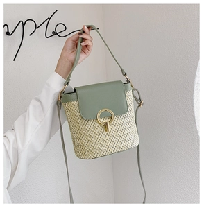 Detail of hand-woven straw bucket bag with green leather trim and golden metal lock