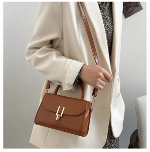 Close-up of caramel leather crossbody bag with gold metal buckle on a white blazer
