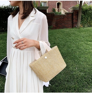 Close-up of handwoven straw tote bag with white fabric handles and decorative button