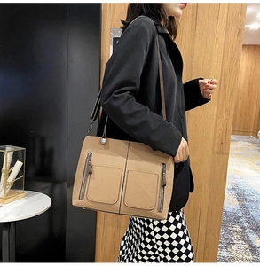 Close-up of khaki tote bag featuring dual front pockets and side vertical zipper accents