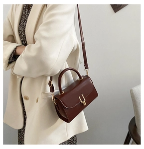 Detail of vintage dark brown crossbody bag with gold H-buckle on a stylish coat