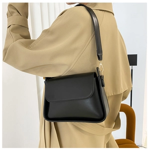 Detail of minimalist black leather baguette bag worn with a classic khaki trench coat