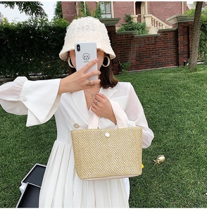 Close-up of beige woven straw tote bag with white round button and ribbon handle