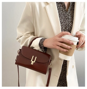 Detail of dark brown leather handbag with gold metal clasp on a stylish cream blazer