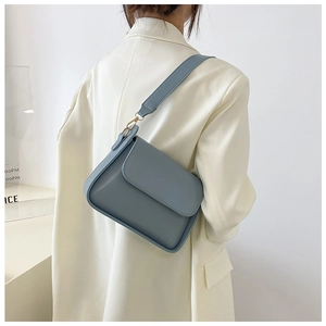 Detail of light blue minimalist leather baguette bag with gold hardware on white suit