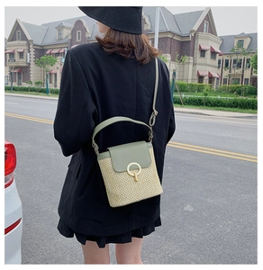 Outdoor street style view of a woven straw bucket bag with green leather details