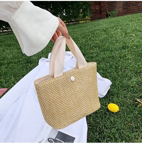 Detailed close-up of woven straw handbag with white ribbon handles and button detail