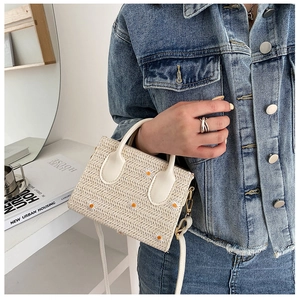 Détail d'un sac en paille avec broderie de marguerites et poignée blanche sur modèle