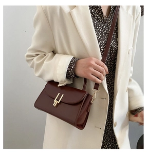 Deep red rectangular handbag with gold metal lock worn over a white suit jacket