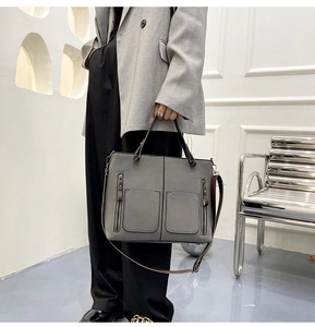 Detail of grey matte leather shoulder bag featuring front pockets and metal zippers