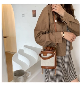 Close-up of canvas bucket bag with brown leather trim and adjustable drawstring closure