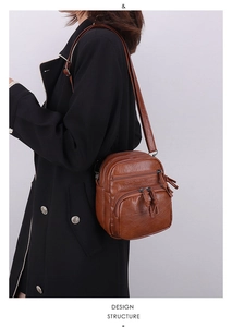 Detail of brown vintage crossbody bag with multiple zip pockets on a black coat
