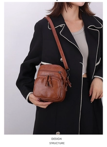 Detail of brown PU leather crossbody bag with triple zippers and tassel accents on a model