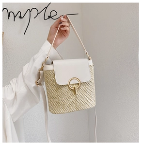 Detail of straw bucket bag featuring a white leather flap and a round gold metal clasp
