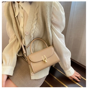 Close-up of beige leather handbag featuring a signature golden H-shaped metal twist lock