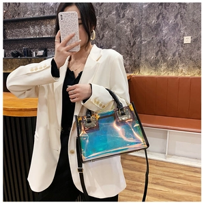 Detail of holographic laser tote bag with black trim and gold buckles on a white blazer