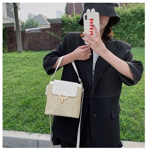 Detail view of woven straw bucket bag with white leather flap and gold metal buckle