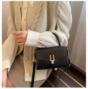 Detail of a black leather crossbody bag featuring a golden geometric twist lock