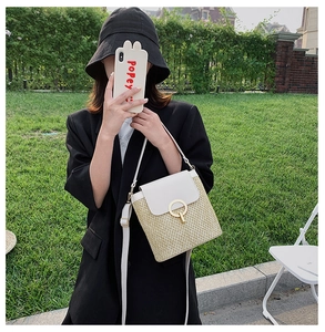Detail of a straw crossbody bucket bag featuring a white leather flap and gold metal ring