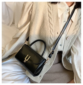 Close-up of black leather crossbody bag with gold buckle and top handle in a lifestyle setting