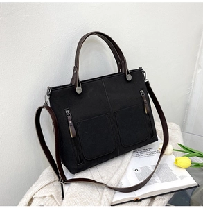 Detail of matte black tote bag with brown handles and two front zipper pockets on white knit