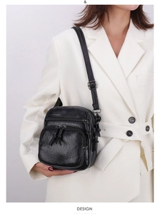 Detail of black multi-zipper crossbody bag in soft pebble leather on a white blazer