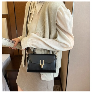 Detail of a vintage black crossbody bag with a gold lock and slim shoulder strap