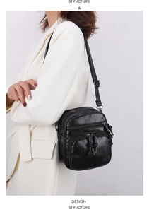 Detail of black multi-zipper PU leather crossbody bag with adjustable strap on white blazer