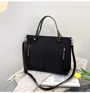 Detail of black matte tote bag with brown leather handles and dual front pockets