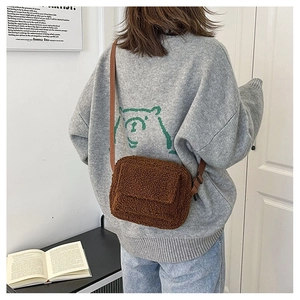 Gros plan du sac bandoulière marron en peluche avec rabat et sangle sur un modèle féminin
