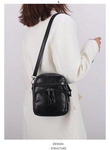 Detail view of the black crossbody bag showing textured leather and multi-zipper layers
