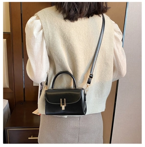 Model wearing black matte leather mini bag with gold buckle and rigid handle