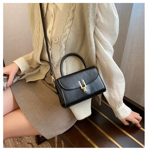 Detail of a vintage black leather crossbody bag with a gold H buckle and slim strap