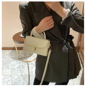 Detail of a creamy white rectangular handbag with a golden H-shaped clasp and handle