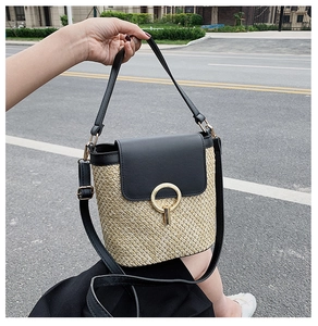 Detail of summer straw bucket bag with black leather trim and round gold buckle hardware