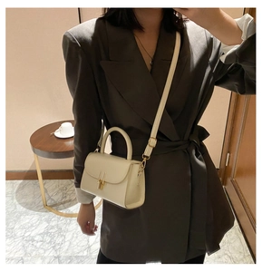 Chic beige crossbody bag with gold buckle worn with a grey blazer in a modern room