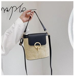 Detailed shot of straw bucket bag with black leather flap and gold circular metal lock